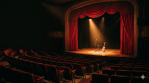 Warm theatre stage with spotlight and rows of empty red seats in an intimate venue